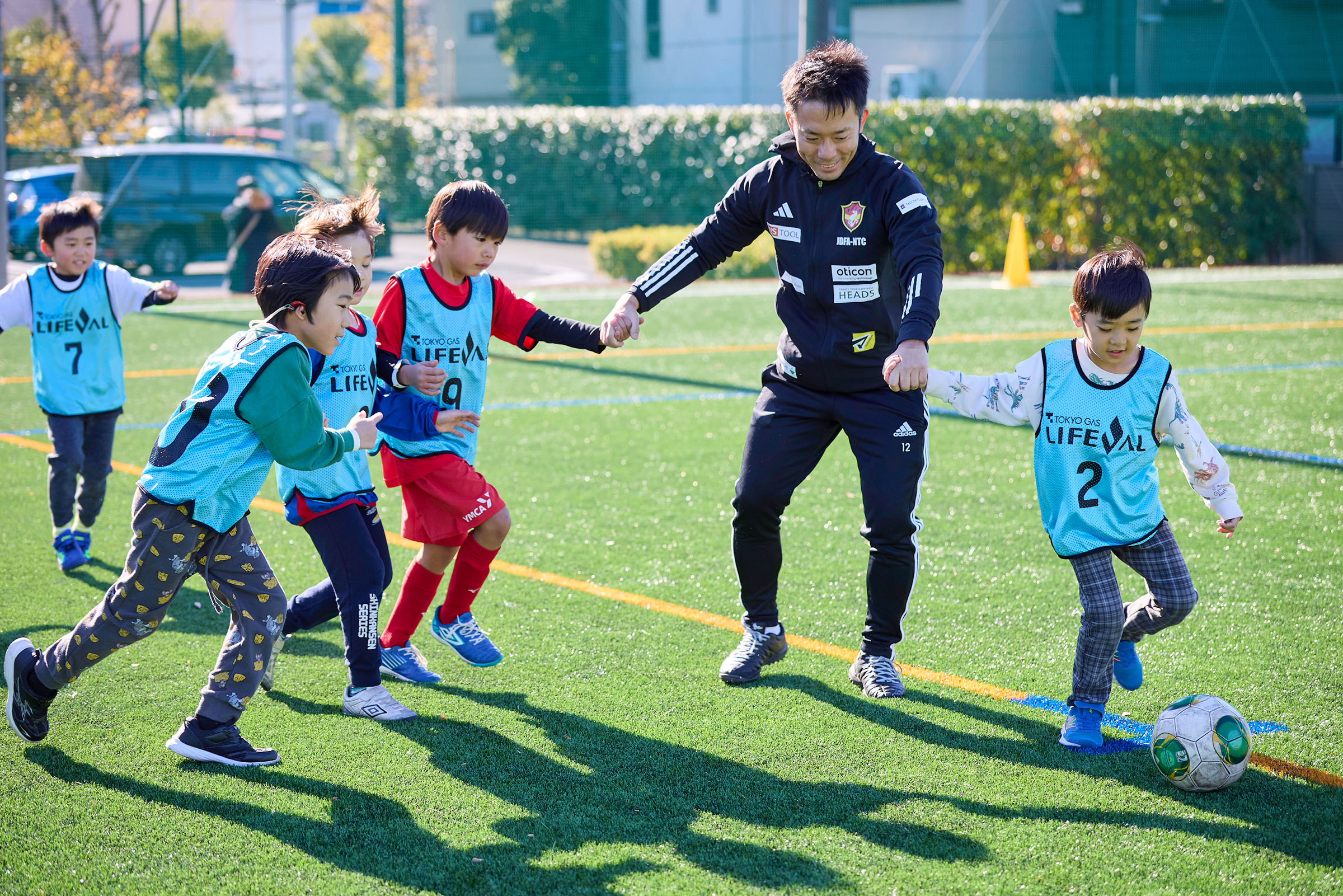 男の子4人と手を繋いでボールを蹴っている折橋選手の写真