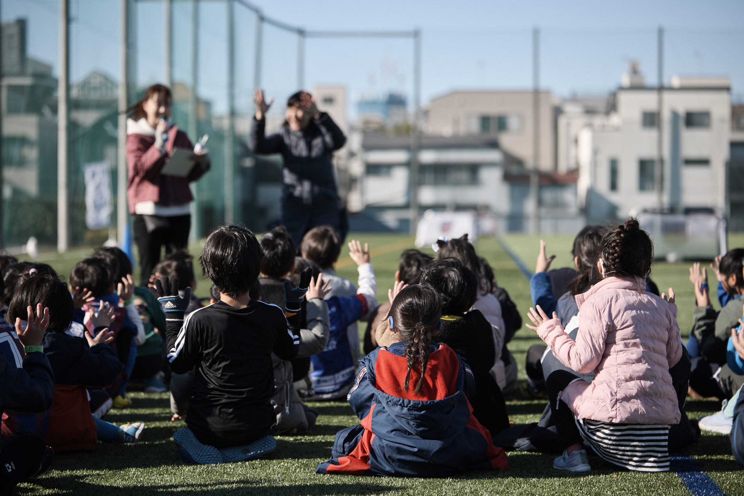 子供たちが芝生の上に座って手話で拍手をしている写真