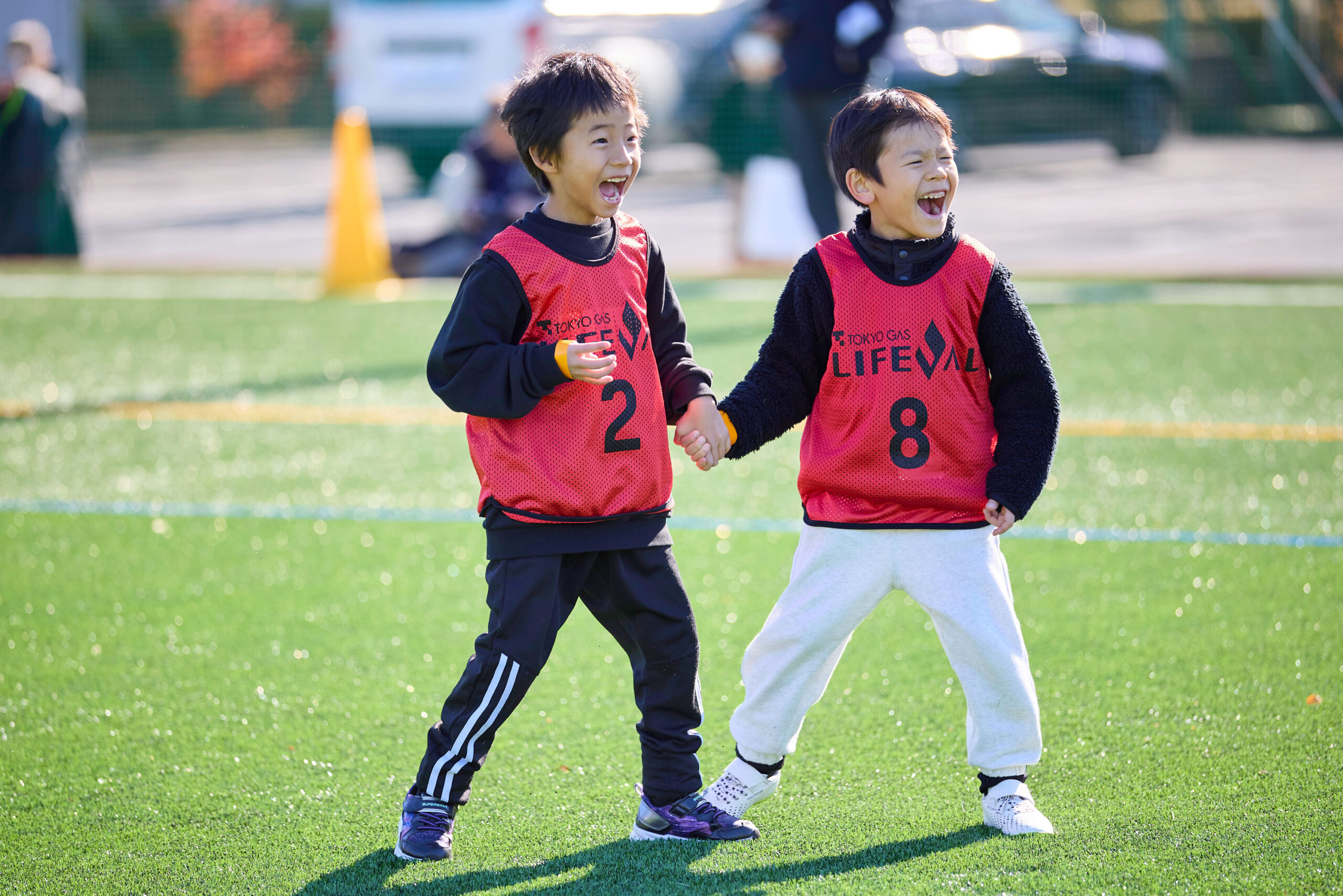 赤いビブスの男の子2人が手を繋いで笑っている写真