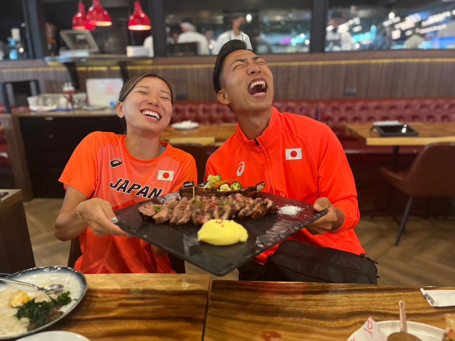 The photo of Takahashi and Maruyama smiling with a steak plate.