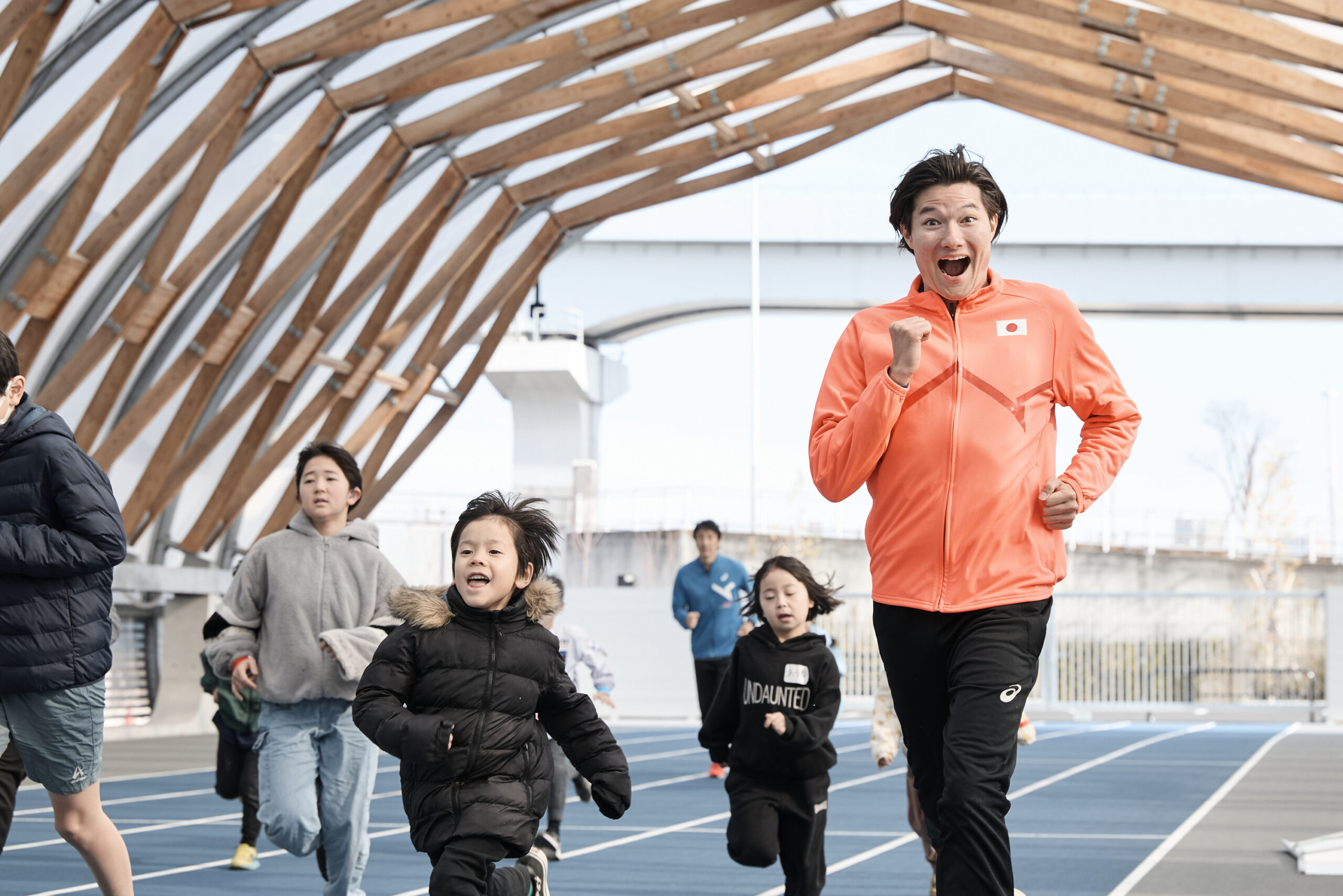 走っている子供たちとカメラ目線の山田選手の写真