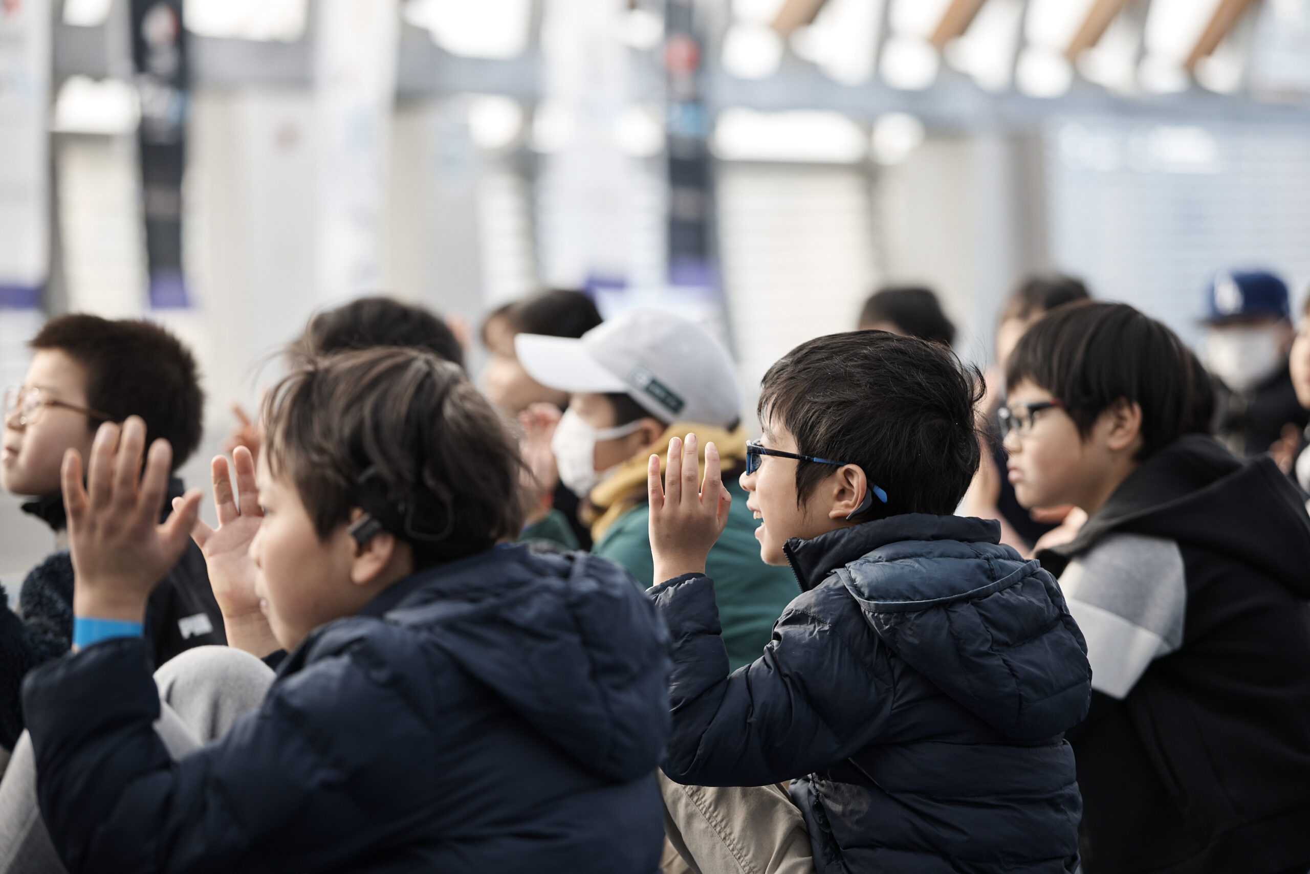 体育座りをしている子供たちが手話の拍手をしている写真