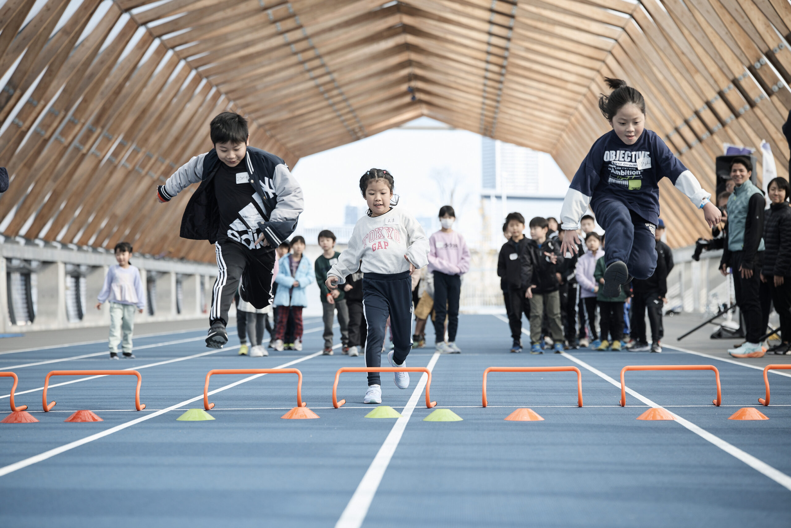 子供たちがミニハードルとマーカーコーンを飛び越えている写真