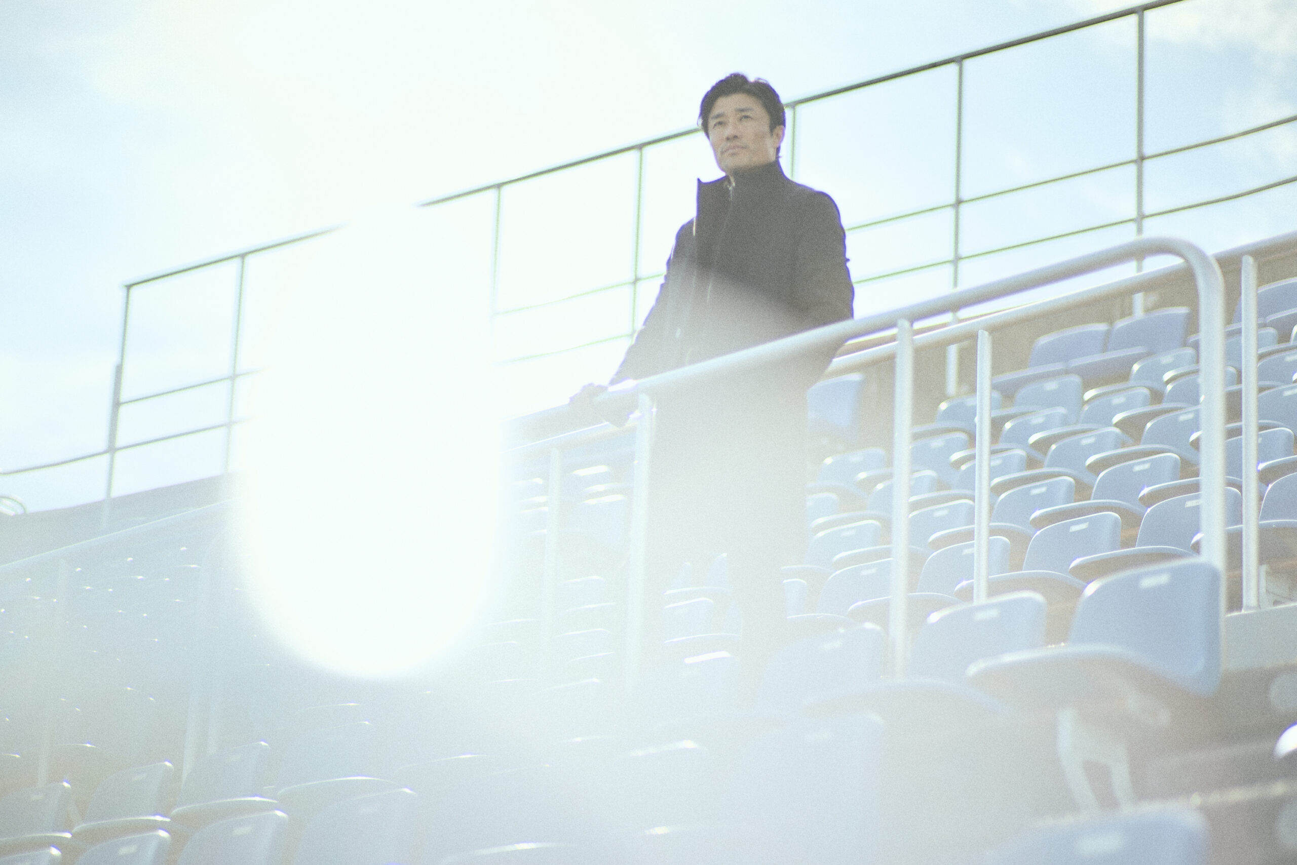 A photo of Suetsugu staring into the distance with his hands on the handrail in the spectator's stands