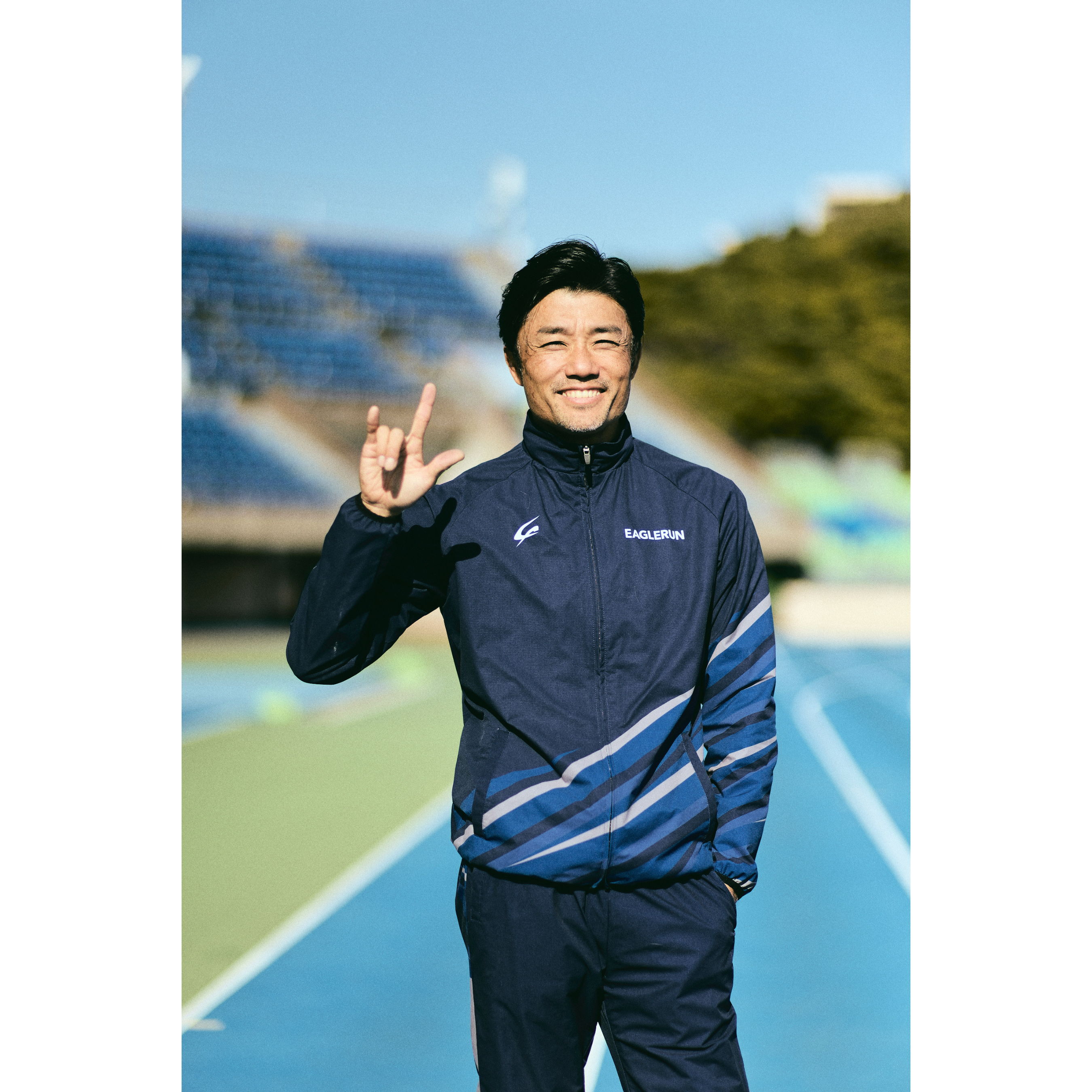 Photo of Suetsugu on the track with his left hand in his pocket and his right hand looking at us with his thumb, index finger, and pinky finger raised.