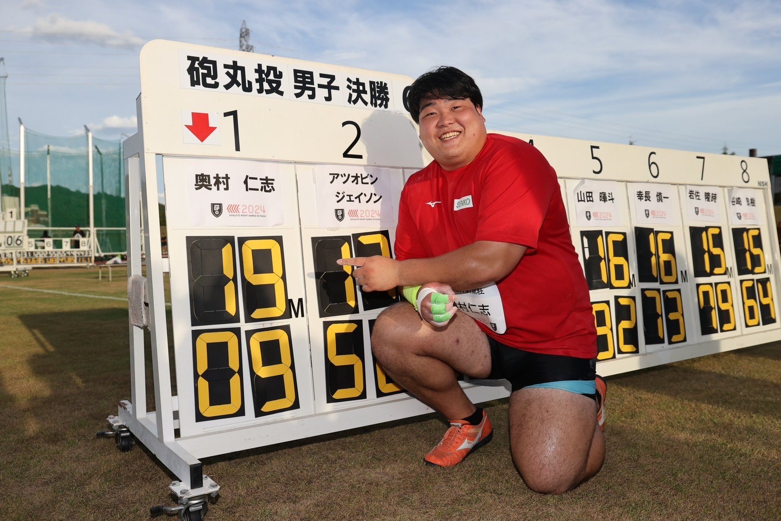 自分の記録を指さしながら笑顔の奥村選手の写真