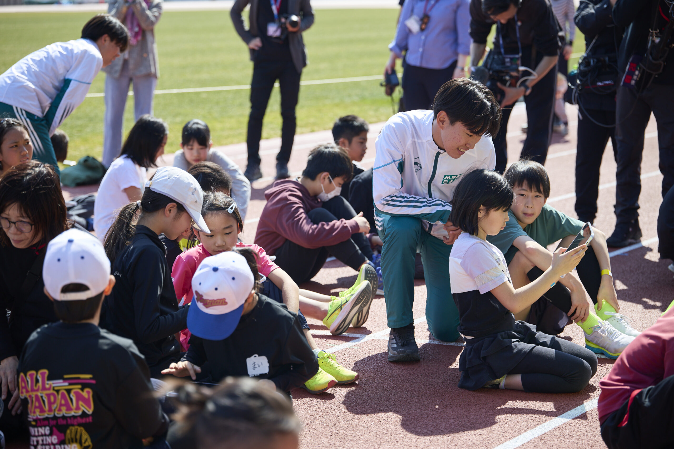 タブレットを操作している参加者に話しかけている青学の選手たちの写真