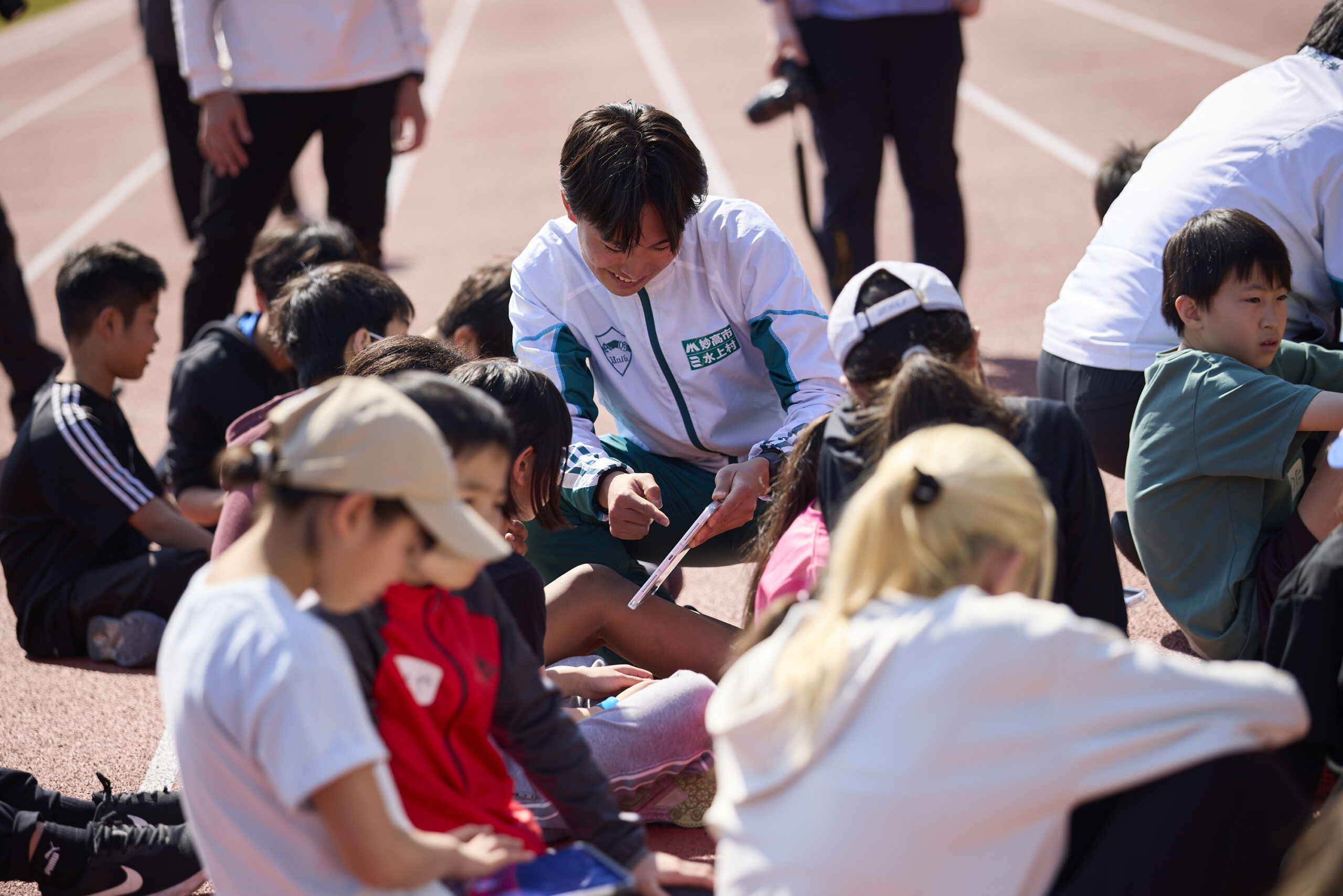 参加者にタブレットを見せて説明している青学選手の写真