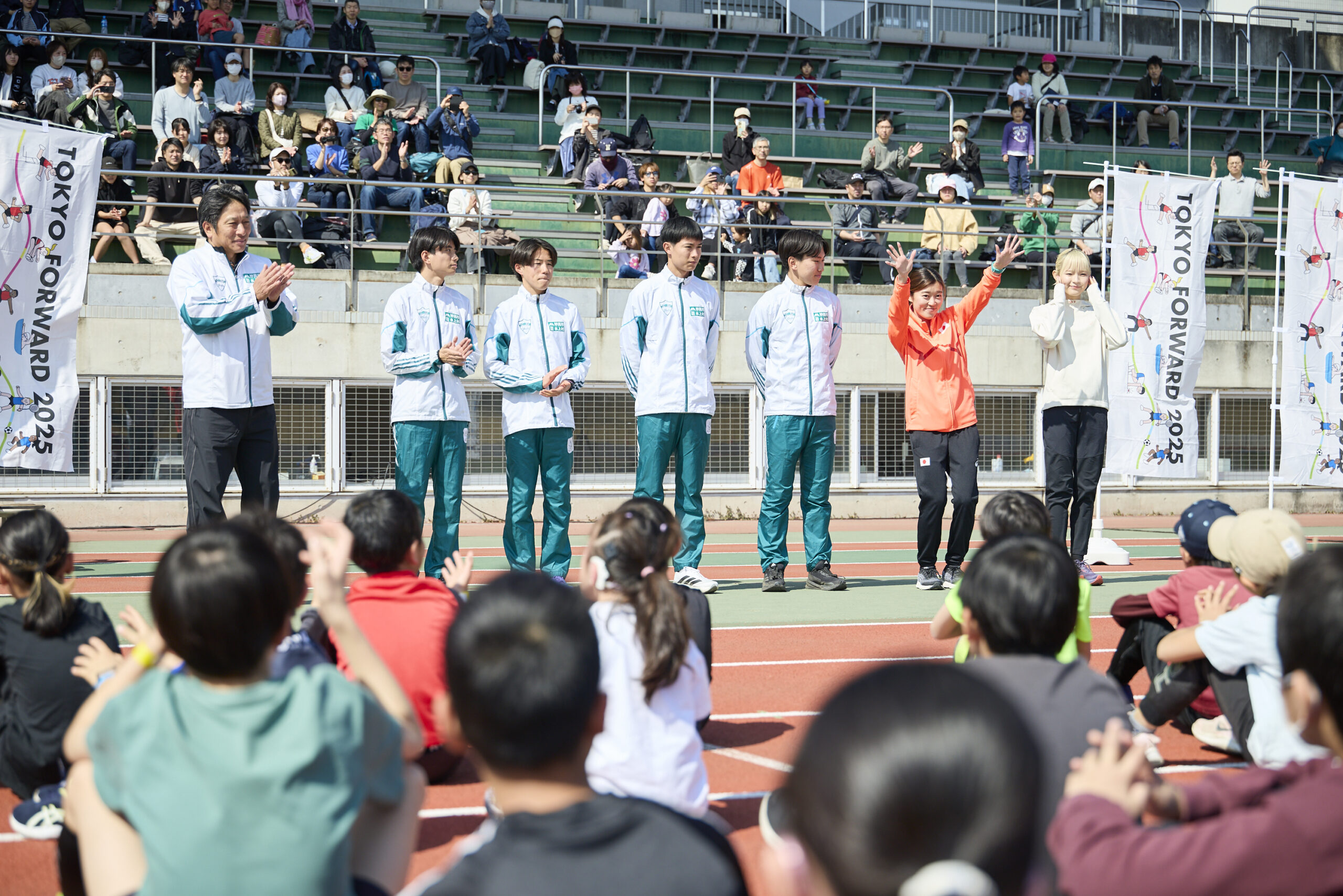 登壇者7名の写真、岡田選手が両手を上げて挨拶をしている。